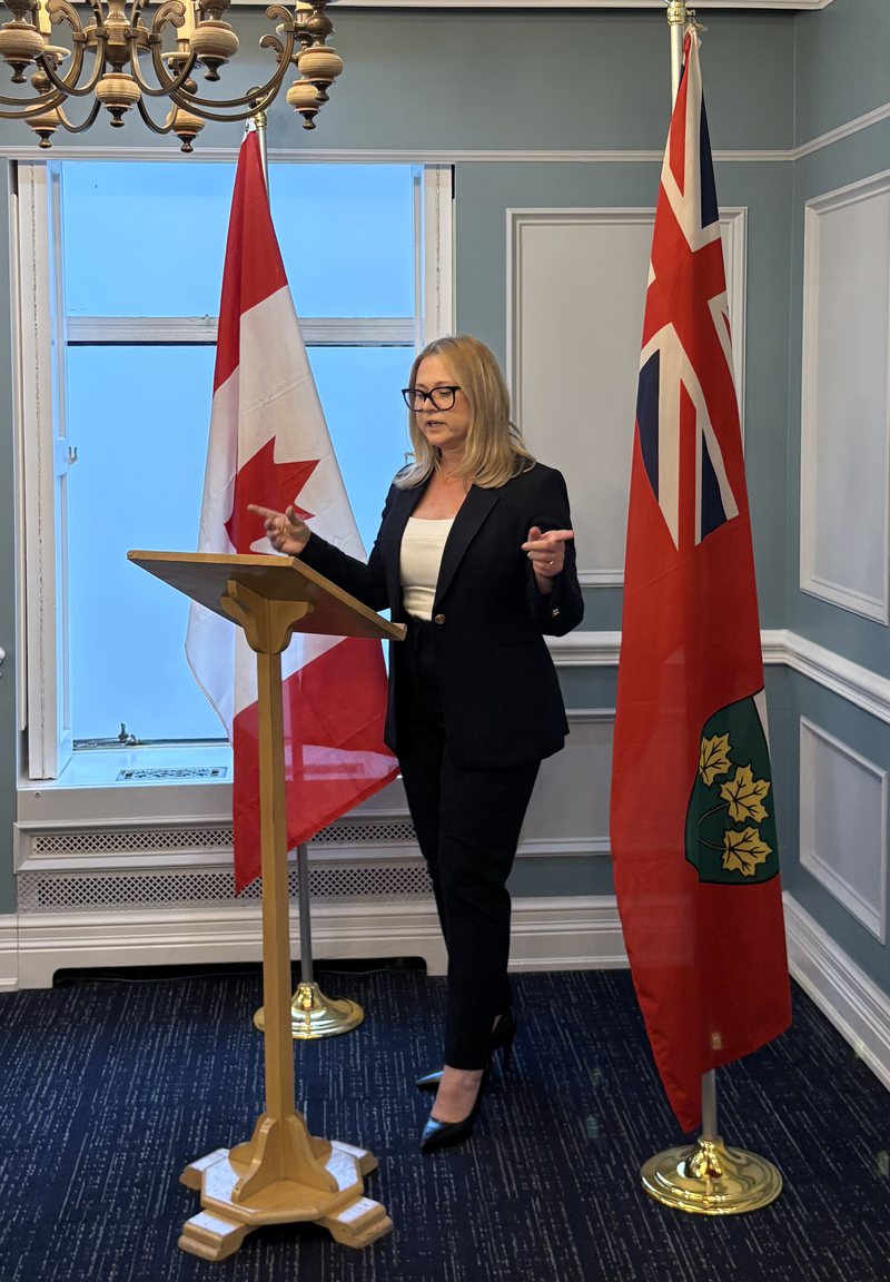Liz Grade speaking at a podium between the Canadian and Ontario flags