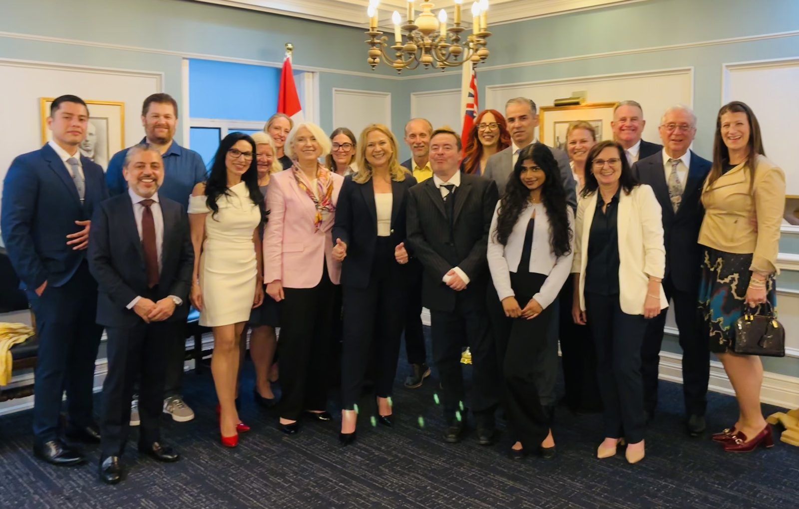 Liz Grade with a group of attendees gathered indoors beneath the Canadian and Ontario flags